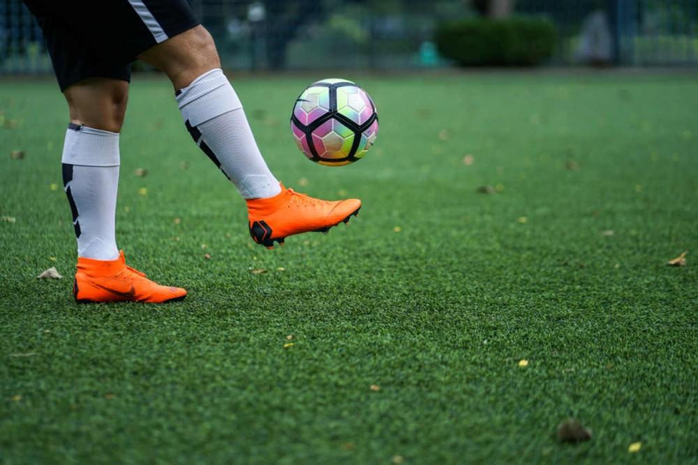 a soccer player plays soccer with orange soccer cleats